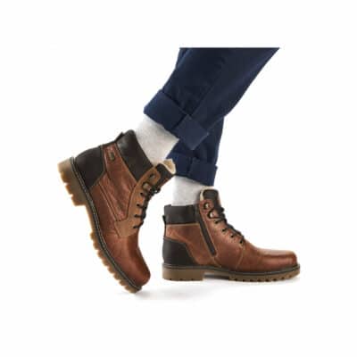 En person går selvsikkert i Rieker Støvle Herre, lavet af brunt læder med sorte accenter og solbrune såler. Støvlerne er snøret i sort, der passer perfekt til marineblå bukser og lysegrå sokker.